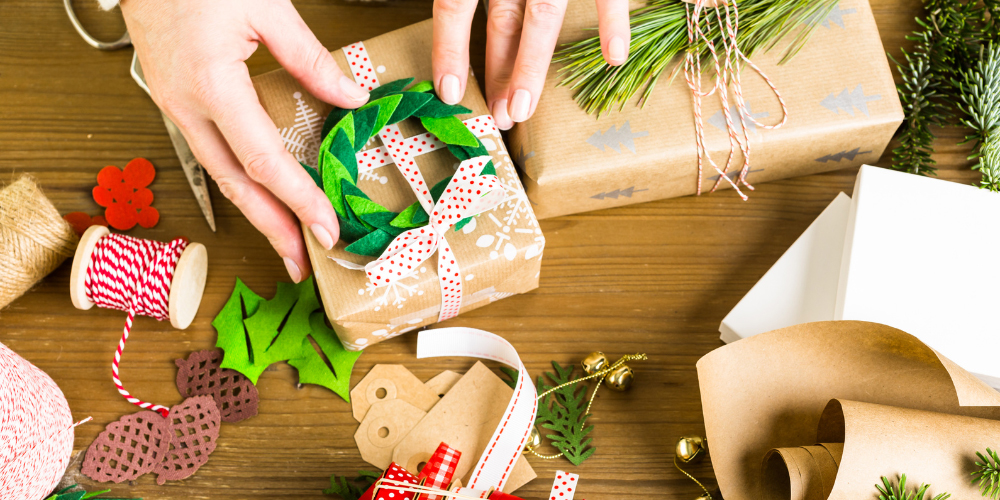 a person's hands putting a felt wreath on a brown paper package. 