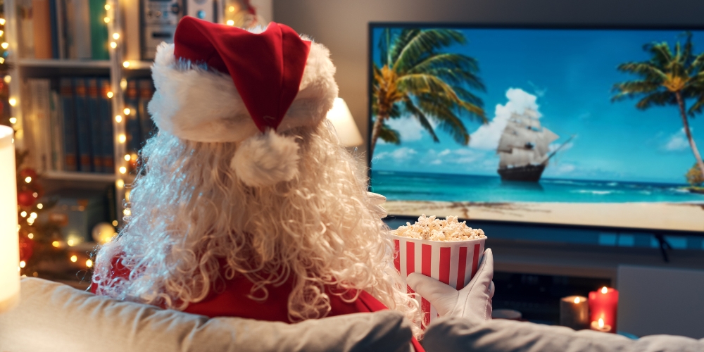 Santa holding a bag of popcorn and watching a large screen TV