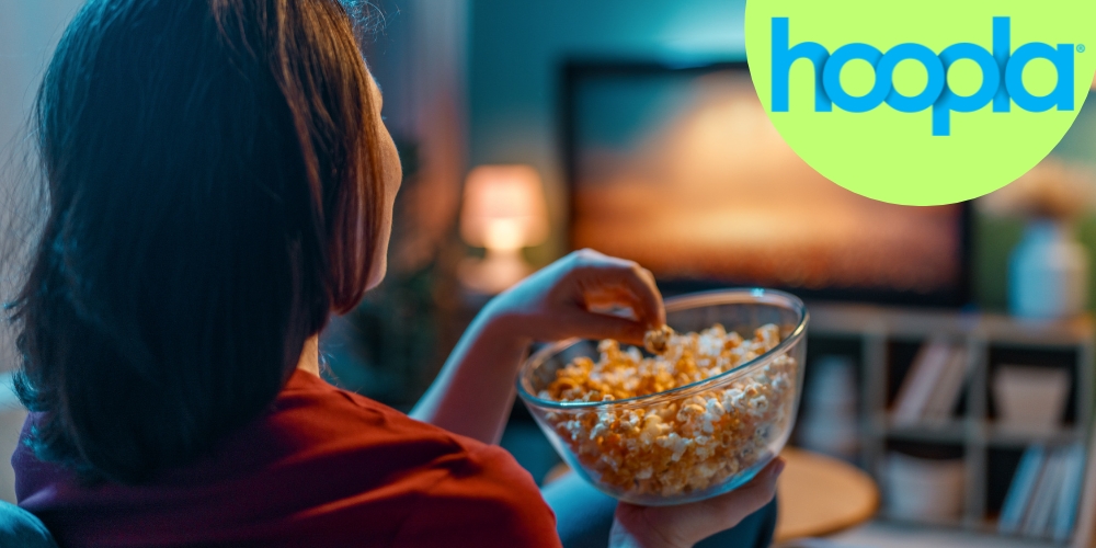 adult sitting on a sofa holding a bowl of popcorn while watching a television 