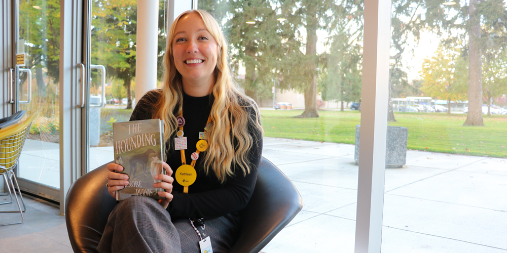 Librarian Kathleen seated and holding the book entitled The Hounding
