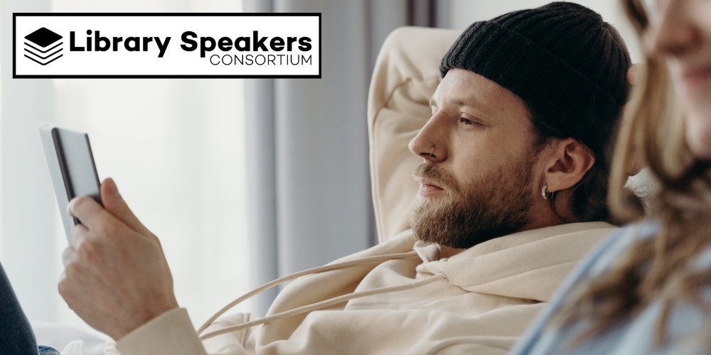 bearded adult wearing a watch cap and looking at a device beside Library Speakers Consortium logo