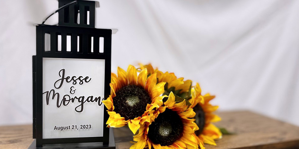 decorative lantern with a vinyl printed insert of the couple's names, situated on a table with a sunflower bouquet