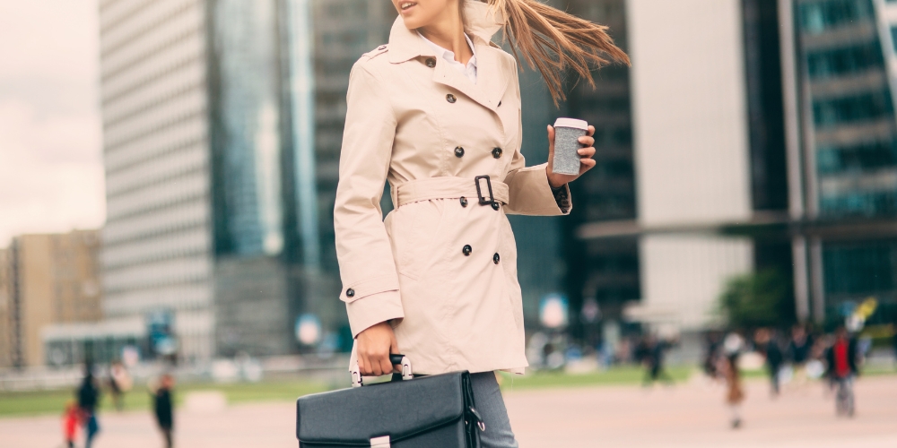 young adult carrying a beverage and an attache case walking in a city