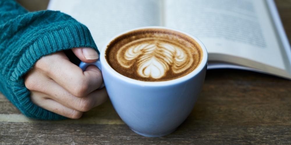 gloved hand resting on a table holding a hot drink with an open book in the background