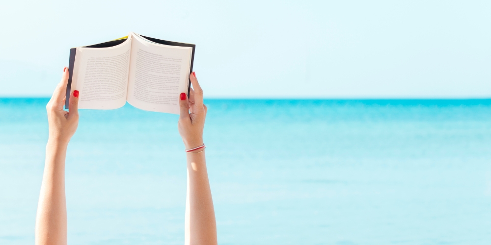 two arms holding up an open book with a lake in the background