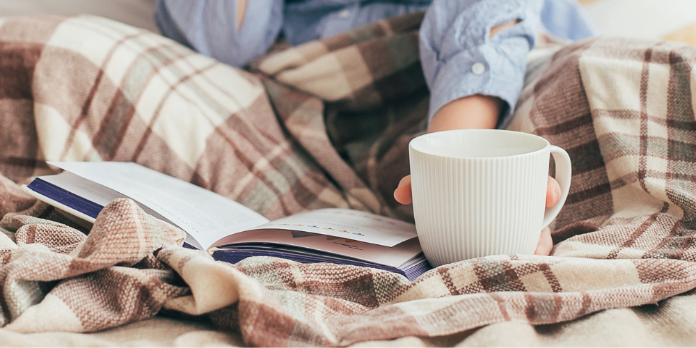 close up view of a book laying on a blanket with mug beside, being held by an adult in the background