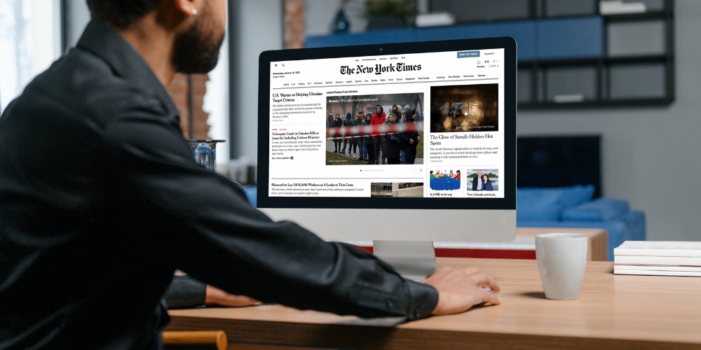 adult sitting at a tale looking at a computer screen displaying the online New York Times newspaper