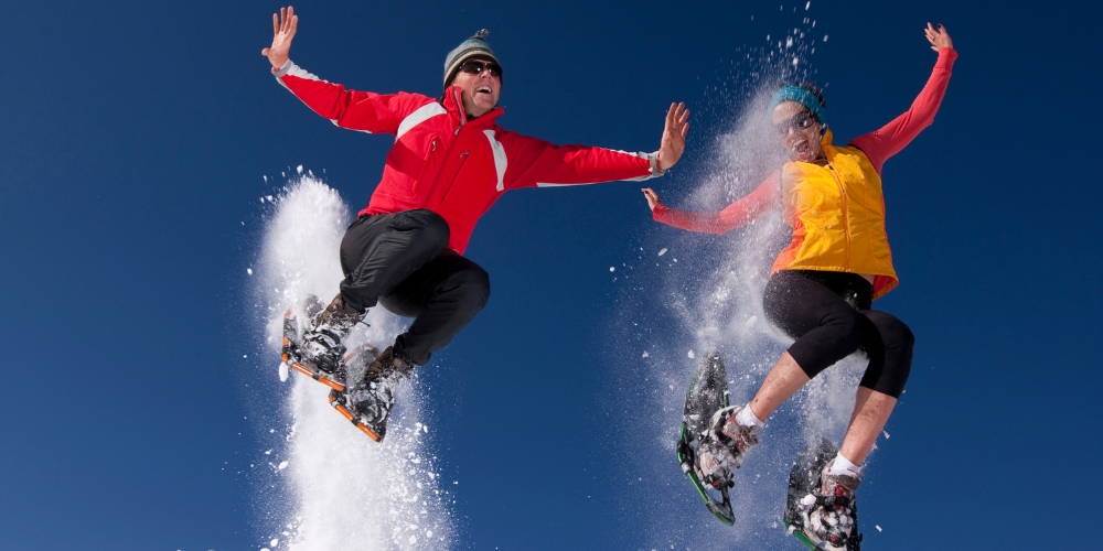two adults wearing snowshoes jumping up