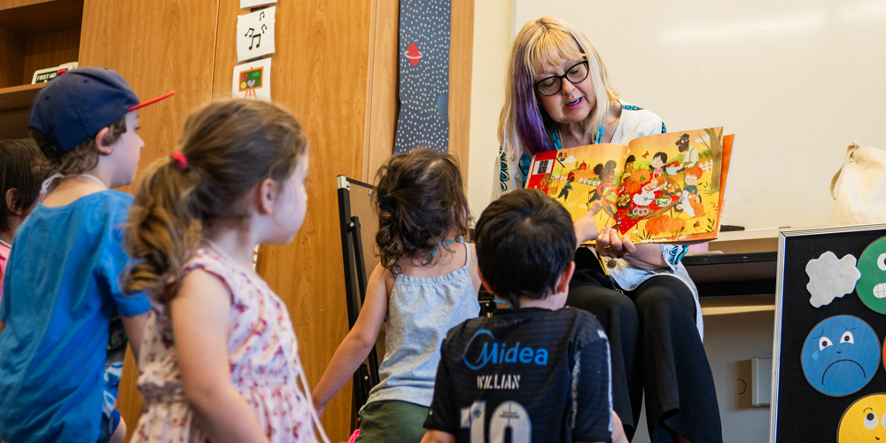 library staff member showing a brightly illustrated book to five children