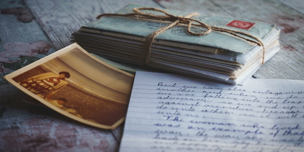 stack of letters bound by string, old colour polaroid photo, handwritten letter on a table