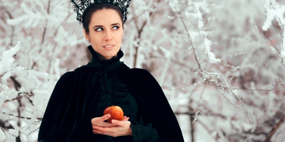 adult wearing a black cape and crown and holding an apple