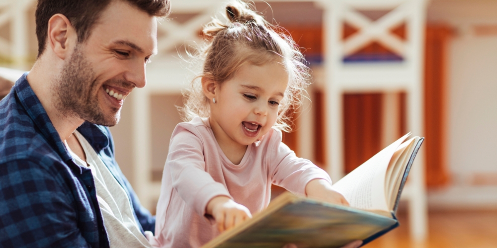 smiling adult sharing a picture book with a baby
