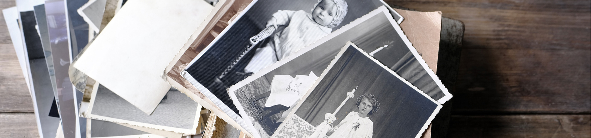 stack of many old photos spread on a table with two black and white photos of children taken about a century ago