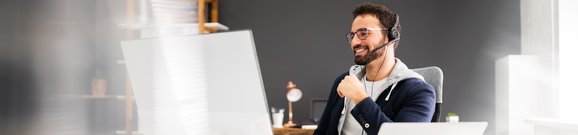 smiling adult wearing headphone and looking at a computer monitor